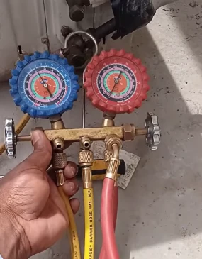 Technician checking AC refrigerant gas pressure with gauges before refill, Bahrain