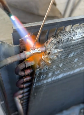 AC technician brazing a copper condenser pipe joint with a torch to seal a refrigerant leak in Bahrain