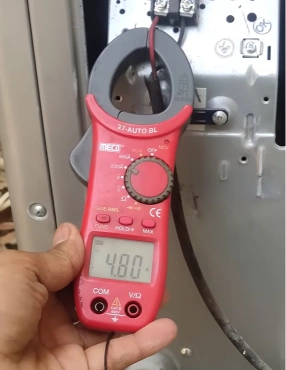 Technician using a clamp meter to check AC compressor electrical current draw during diagnosis in Bahrain